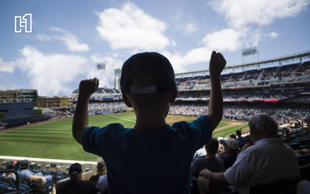 young boy wearing a baseball cap cheers from the stands surrounding a baseball field