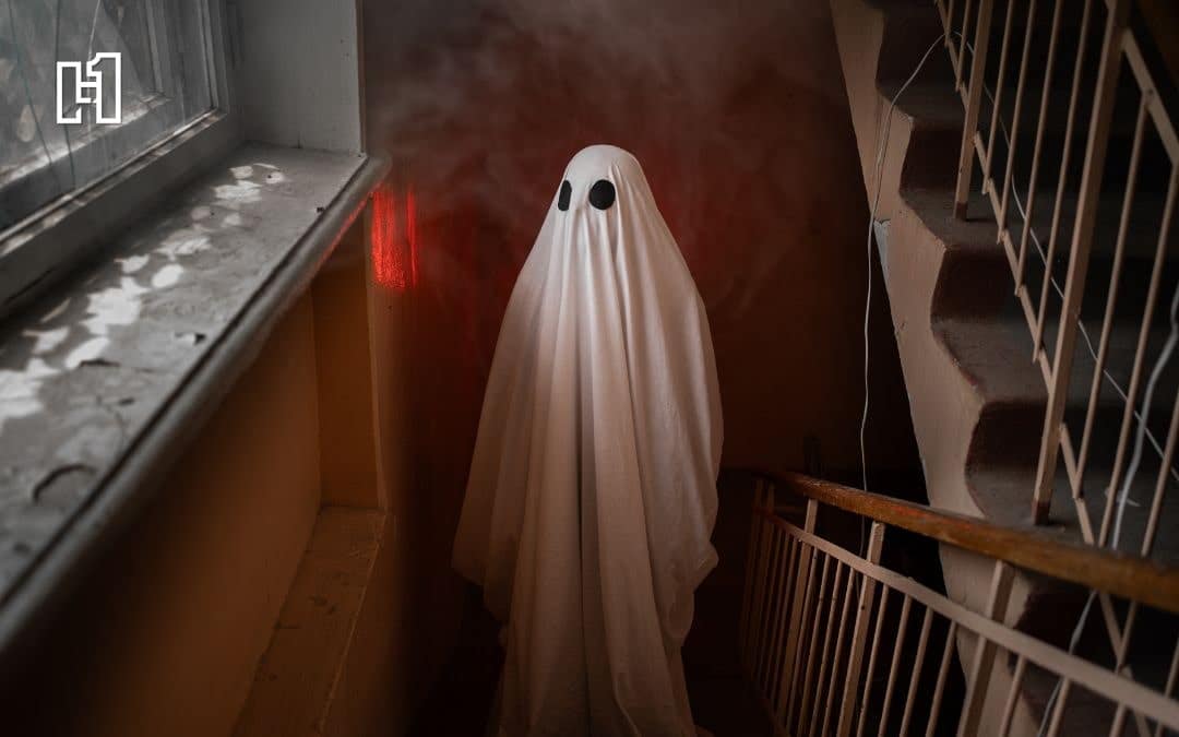 Person dressed as ghost with white bedsheet standing at bottom of stairs