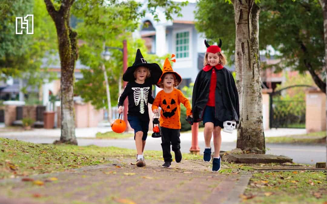 Three children walking down sidewalk dressed in witch, pumpkin, and devil costumes trick-or-treating for Halloween activities in Omaha