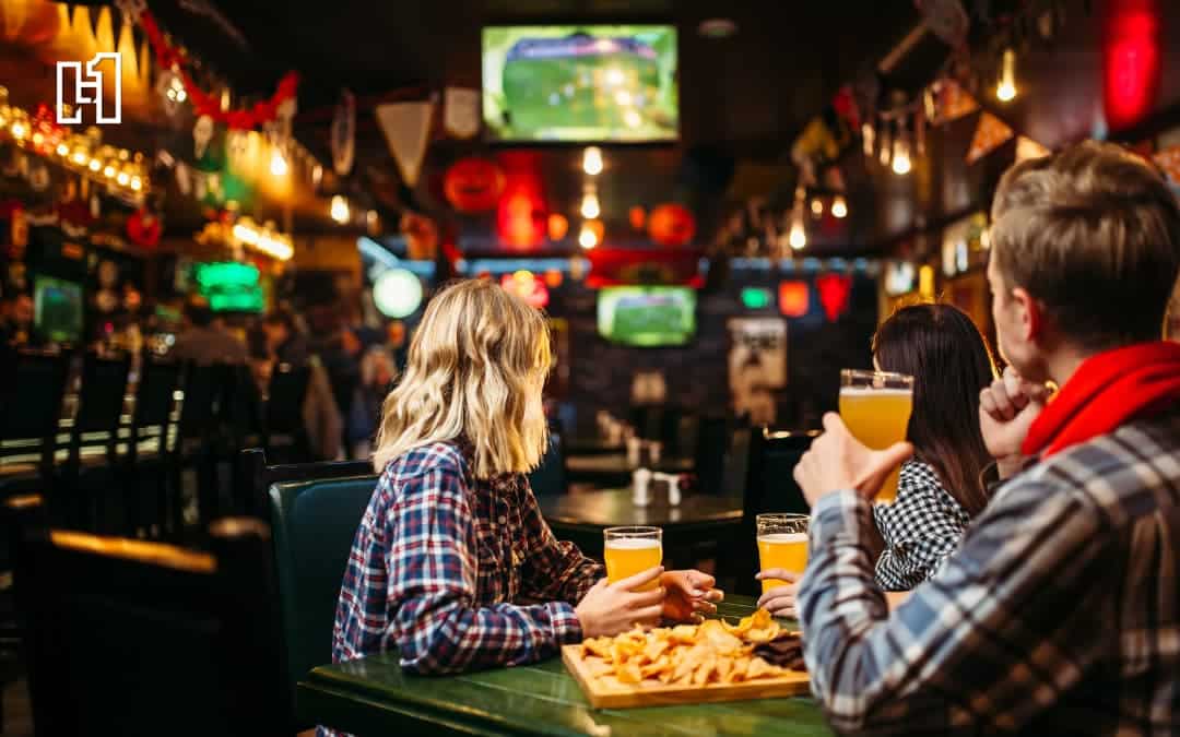 An inside look at a bar with people with drinks in hand and food on the table.
